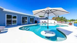 A swimming pool with a sun lounger, a lounge chair, and a large umbrella. - Bayside Retreat with Backyard Oasis (Tampa)