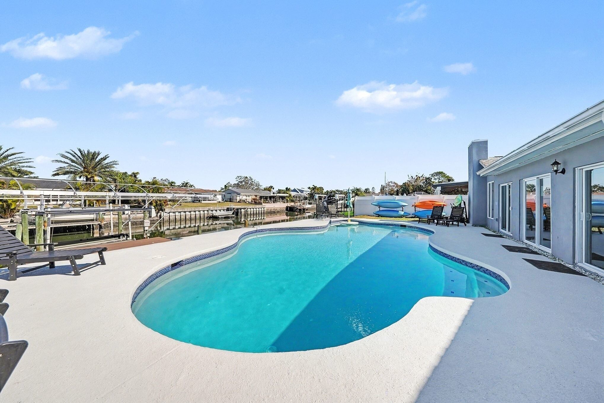 Une piscine à bord incurvé, entourée d’une terrasse blanche et d’un bâtiment doté de grandes fenêtres.