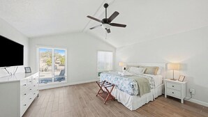 A bedroom with a bed, a ceiling fan, a nightstand, a TV, and a window with blinds. - Bayside Retreat with Backyard Oasis (Tampa)