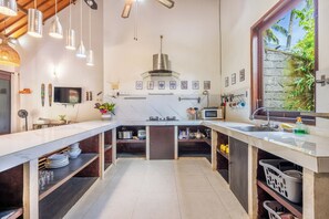 A modern kitchen with a central island, built-in appliances, and a view of greenery outside. - Surya Villa (Karangasem)