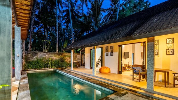 Un área moderna junto a la piscina con una piscina cristalina, una zona de estar cubierta y vistas del paisaje tropical circundante.