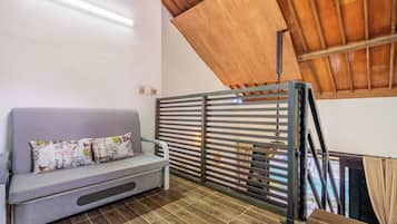 Una habitación con un sofá gris, cojines estampados, un panel divisor de madera con listones y suelo de baldosas.