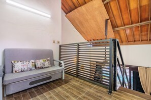 A room with a grey sofa, patterned cushions, a wooden slatted partition, and a tiled floor.