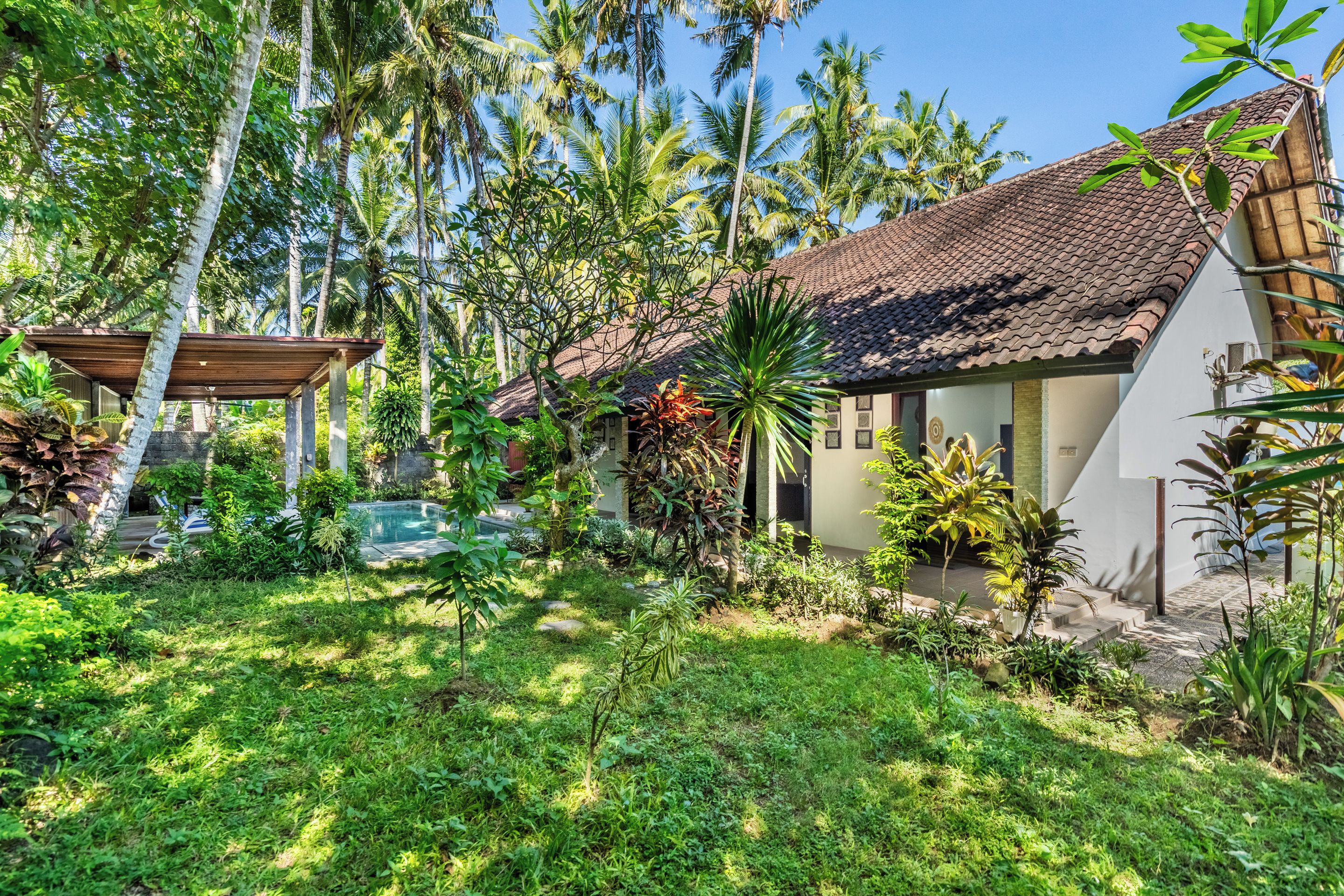 Un jardín tropical con piscina, un pabellón y una casa de techo con tejas.