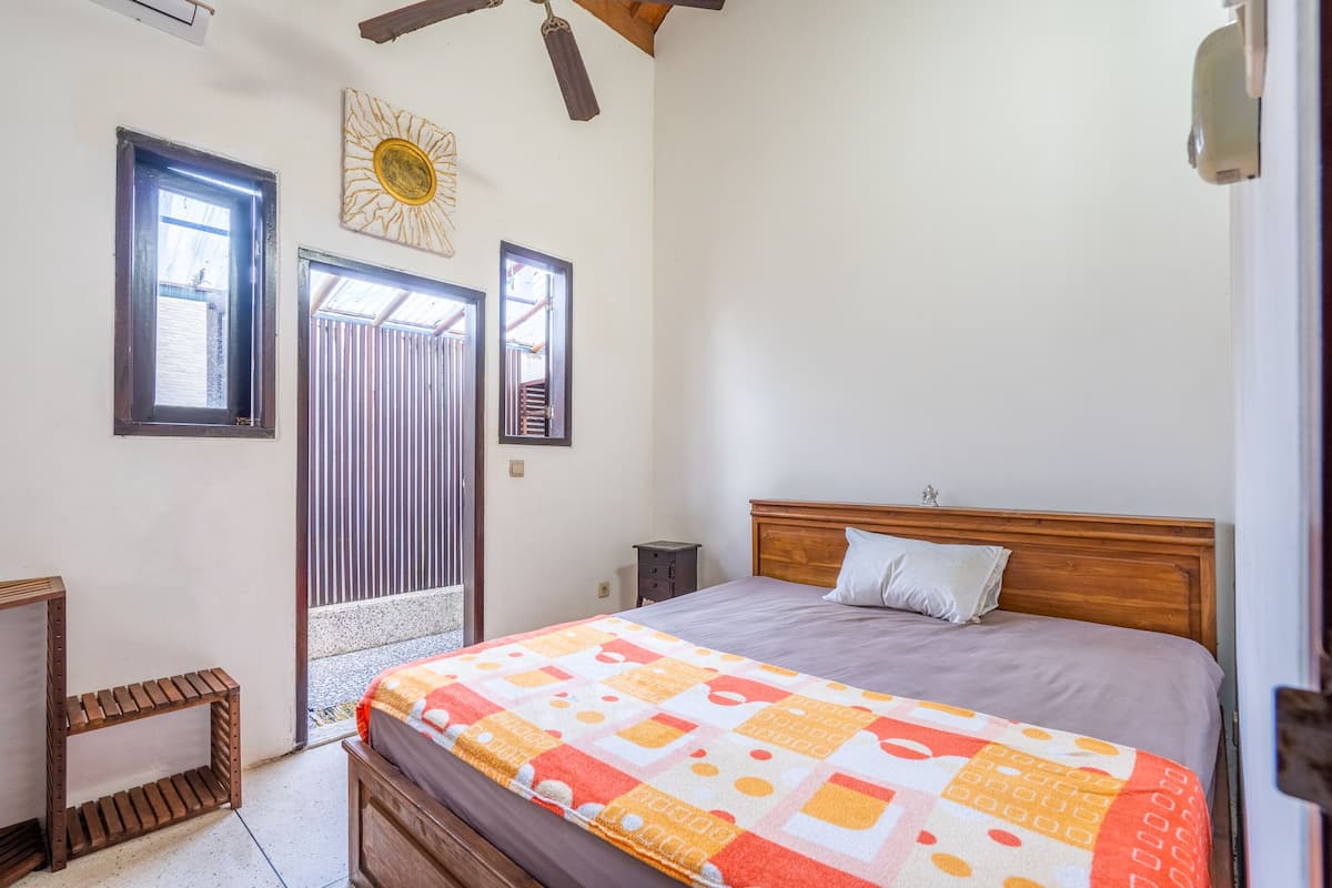 A bedroom with a wooden bed, a nightstand, a small table, and a window with blinds.