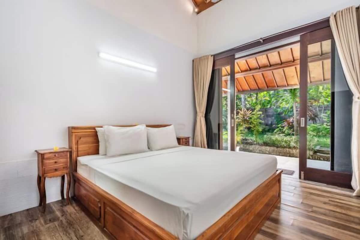 A bedroom with a wooden bed, a nightstand, and a sliding glass door leading to a garden.