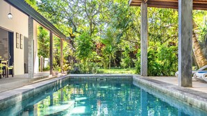A swimming pool with a clear blue water surface, surrounded by lush greenery and a pergola structure. - Surya Villa (Karangasem)