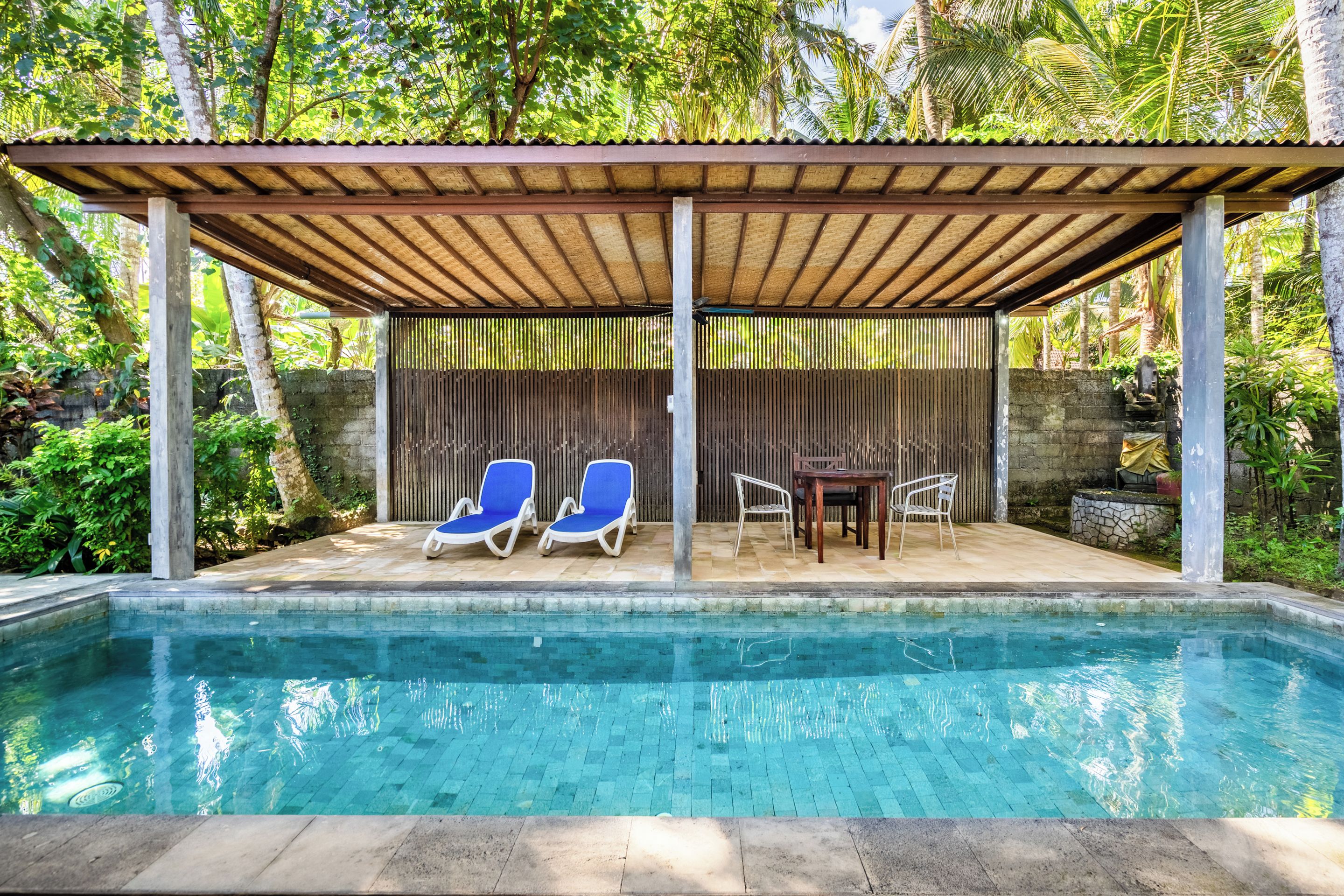 A pool area with a covered seating area, two blue lounge chairs, and a table with chairs.