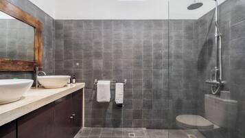 Un baño moderno con un espejo grande, un lavamanos, una ducha y un inodoro.
