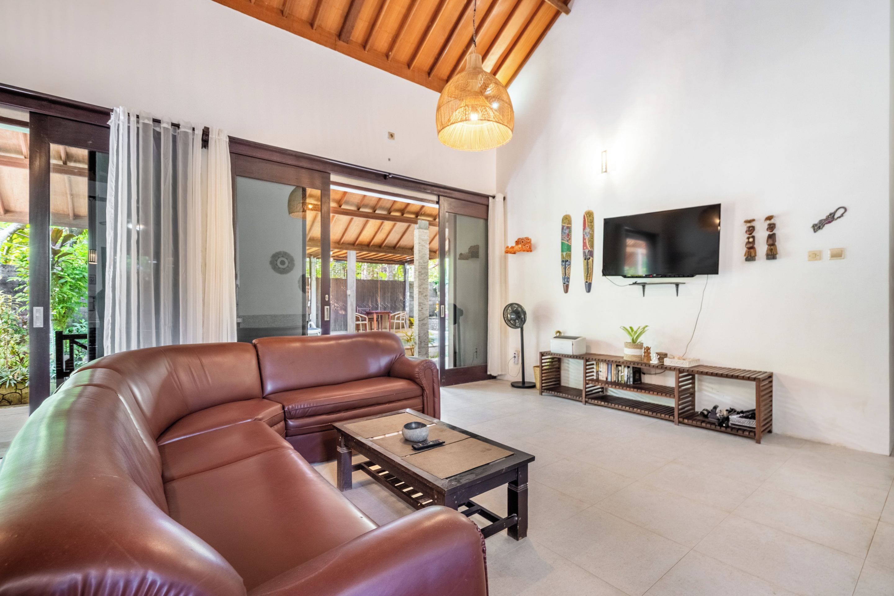 Una sala de estar con un sofá de cuero marrón, una mesa de centro, un televisor y un mueble para televisión con adornos.