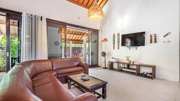 Una sala de estar con un sofá de cuero marrón, una mesa de centro, un televisor y un mueble para televisión con adornos.