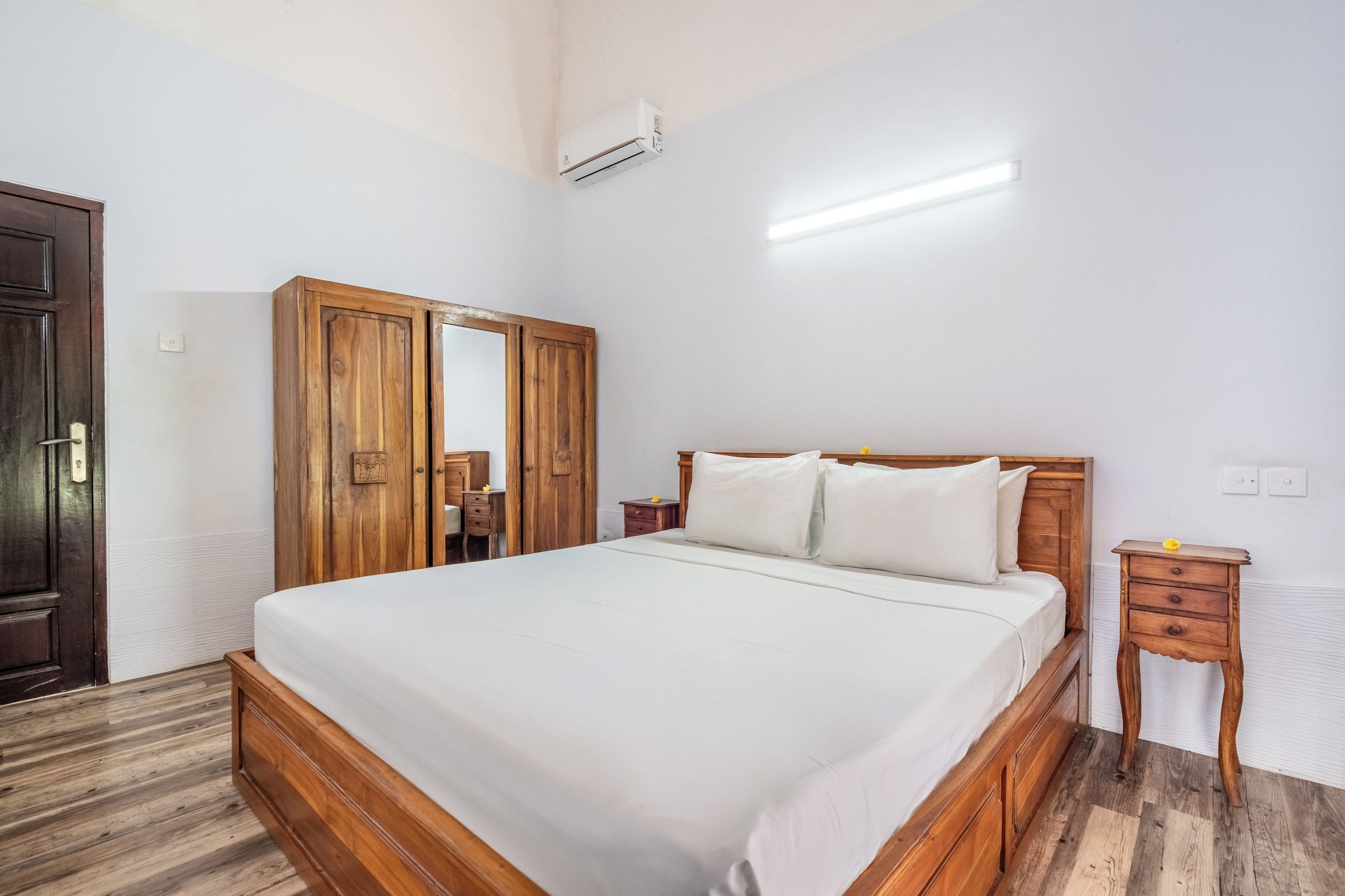 Un dormitorio con cama de madera, armario de madera, mesita de noche y velador.