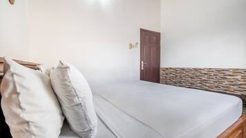 A single bed with a wooden headboard, a white mattress, and two pillows.
