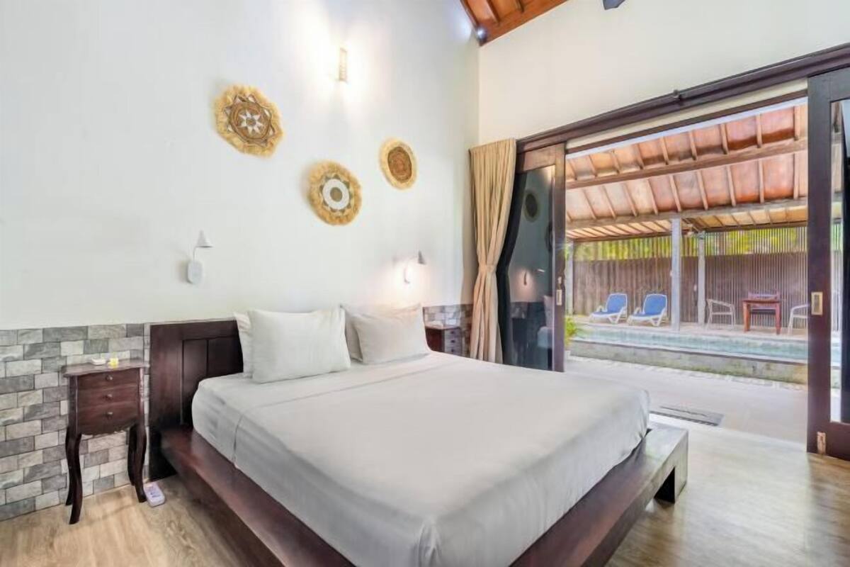 A bedroom with a bed, a nightstand, a wall clock, and a view of an outdoor pool area.