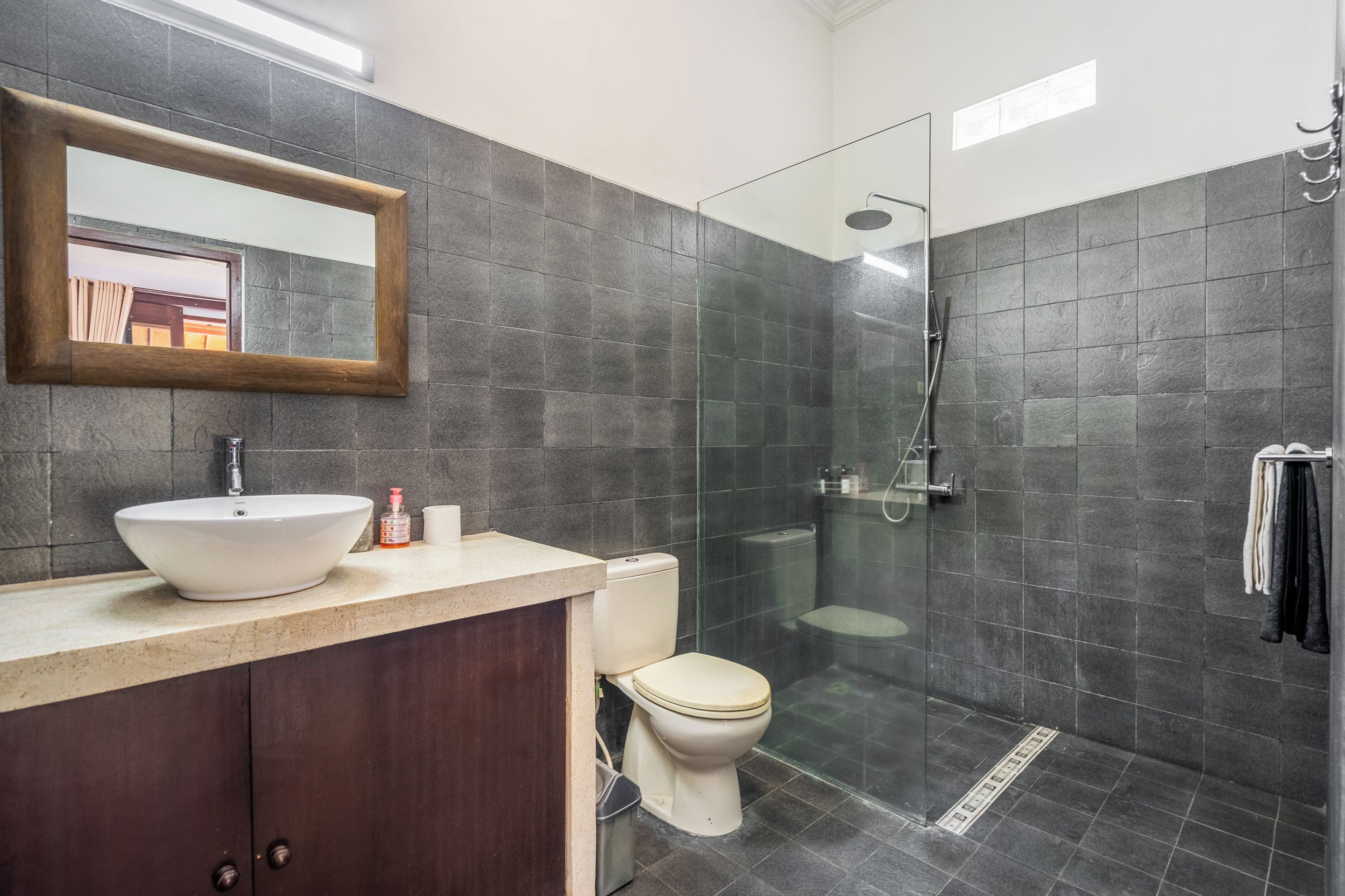 Un baño moderno con un espejo grande, un lavamanos, un inodoro y una zona de ducha con mampara de vidrio.
