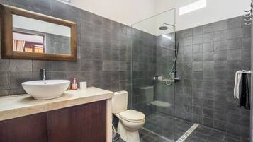 Un baño moderno con un espejo grande, un lavamanos, un inodoro y una zona de ducha con mampara de vidrio.