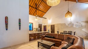 Amplia sala de estar con un sofá de cuero marrón, una mesa de centro y un comedor con mesa y sillas de madera.