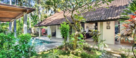 A house with a tiled roof, a swimming pool, and lush greenery.