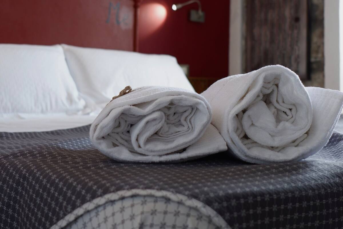 A neatly made bed with rolled towels, a red wall, and a wooden door in the background.