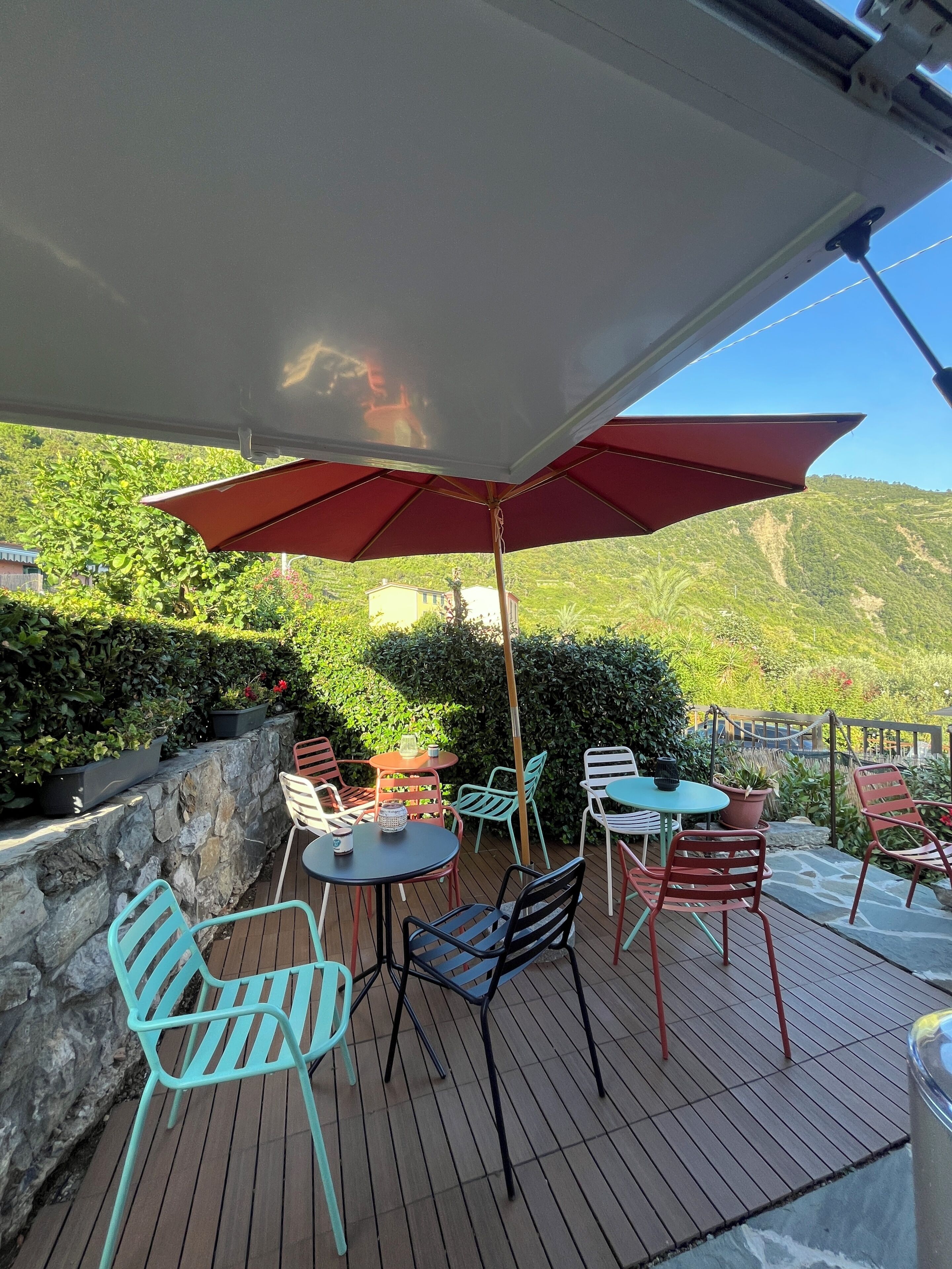 Un patio al aire libre con mesas y sillas, un muro de piedra y vistas a colinas verdes.