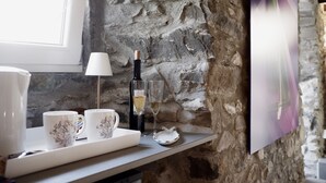 A stone wall interior with a table displaying a wine bottle, glasses, and decorative items. - Madüneta 5 Terre Guesthouse (Vernazza)