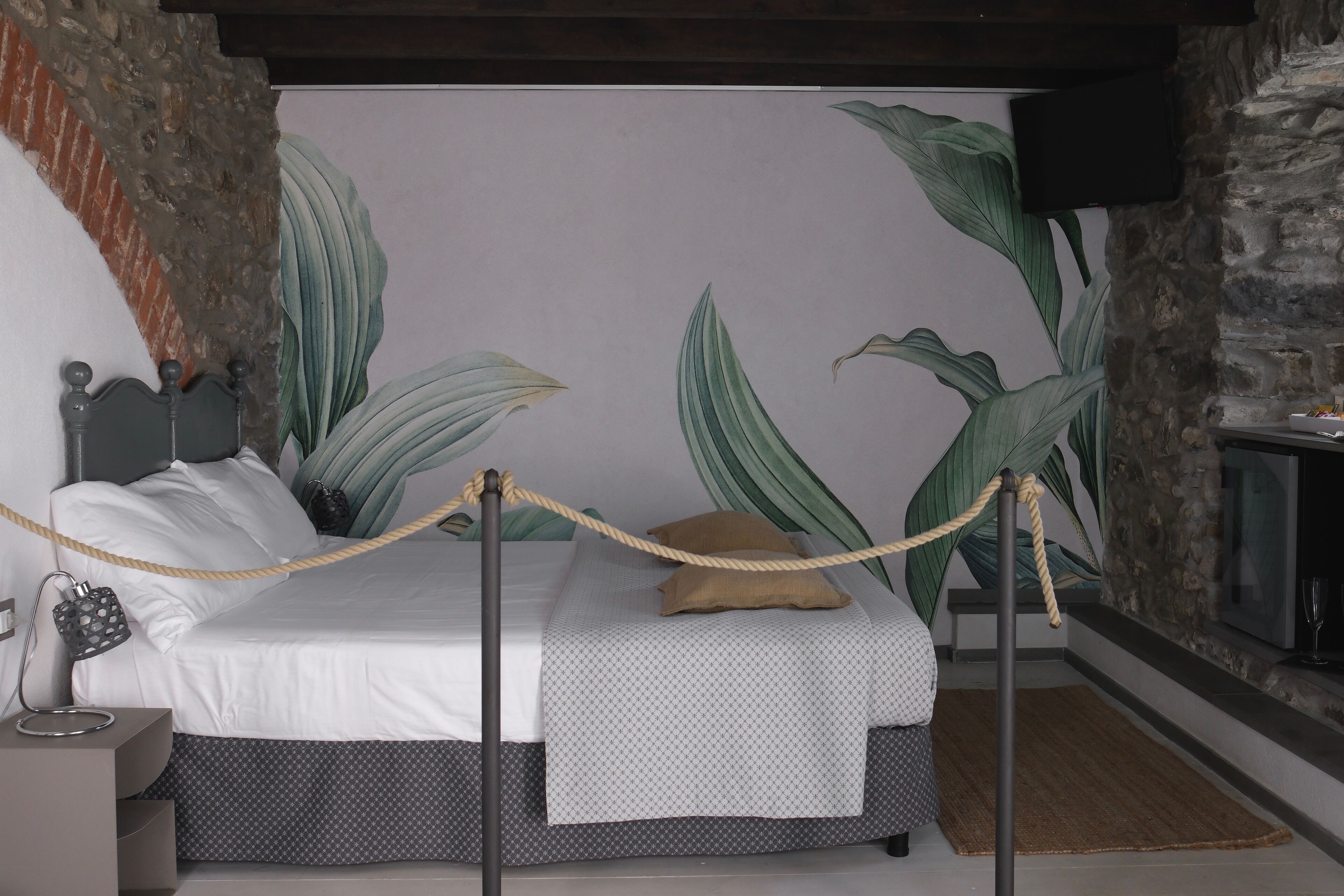 Une chambre à coucher avec un lit, une table de chevet, un téléviseur fixé au mur, qui est en pierre, et une grande plante.