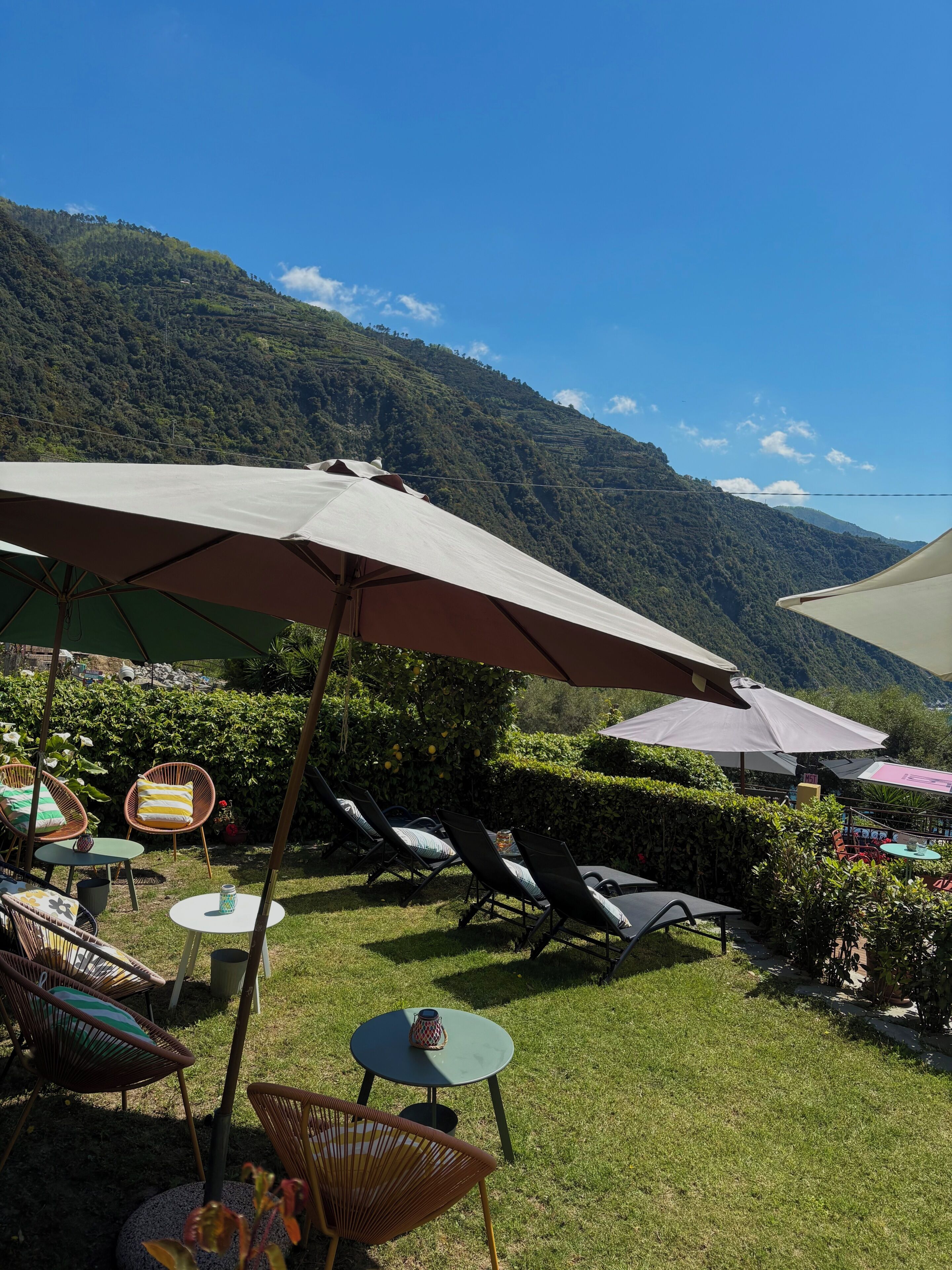 An outdoor seating area with umbrellas, chairs, and tables, overlooking a mountainous landscape.