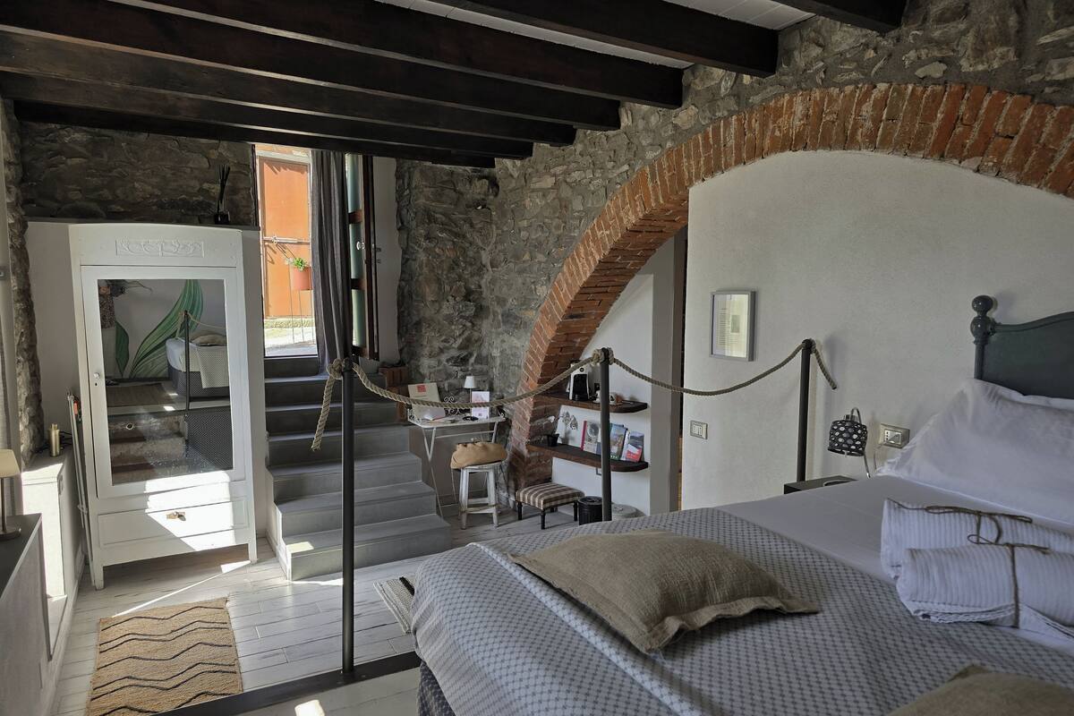A bedroom with a bed, a desk, and a chair. There is a staircase leading to another room.