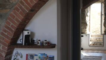 A cozy room with a brick archway, a shelf with books and a kettle, a bench, and a trash bin.