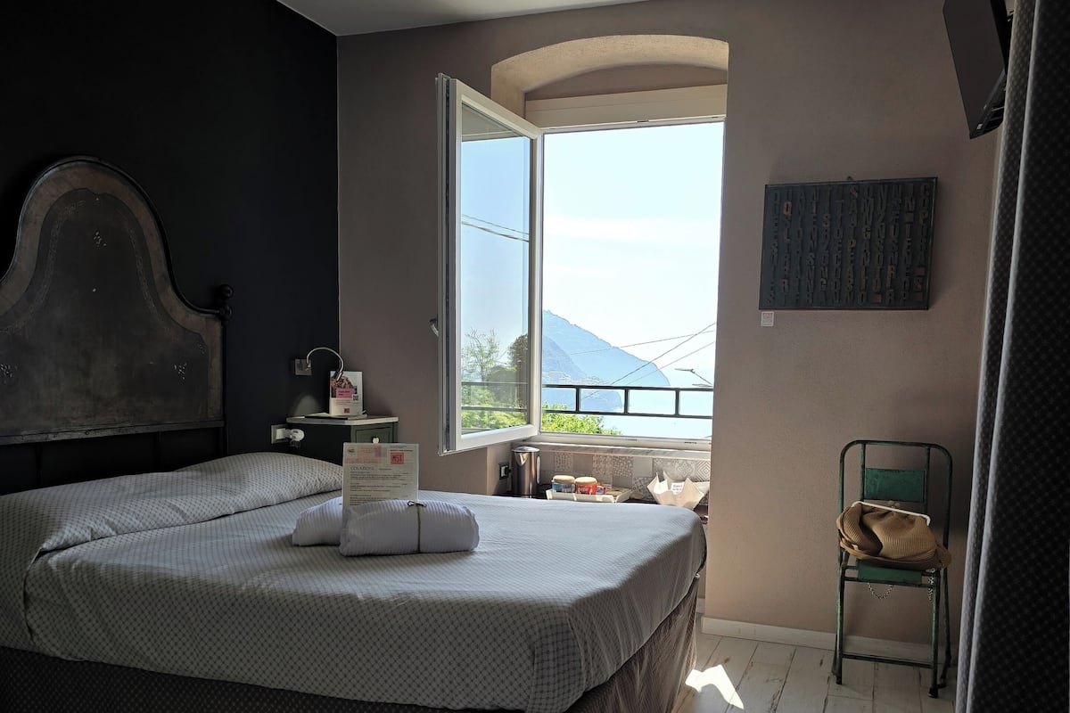 A bedroom with a large bed, a chair, a small table, and a window with a view of the outdoors.