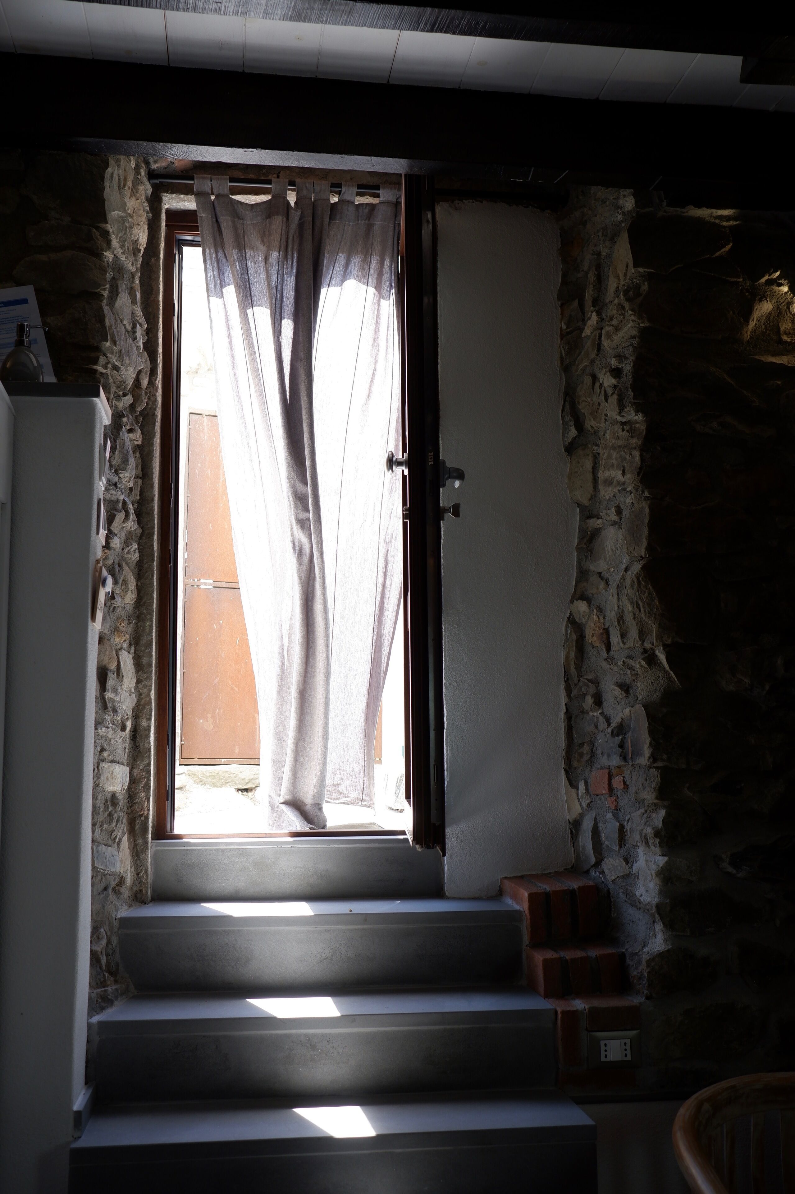 A staircase leading to a room with a stone wall and a window with curtains.