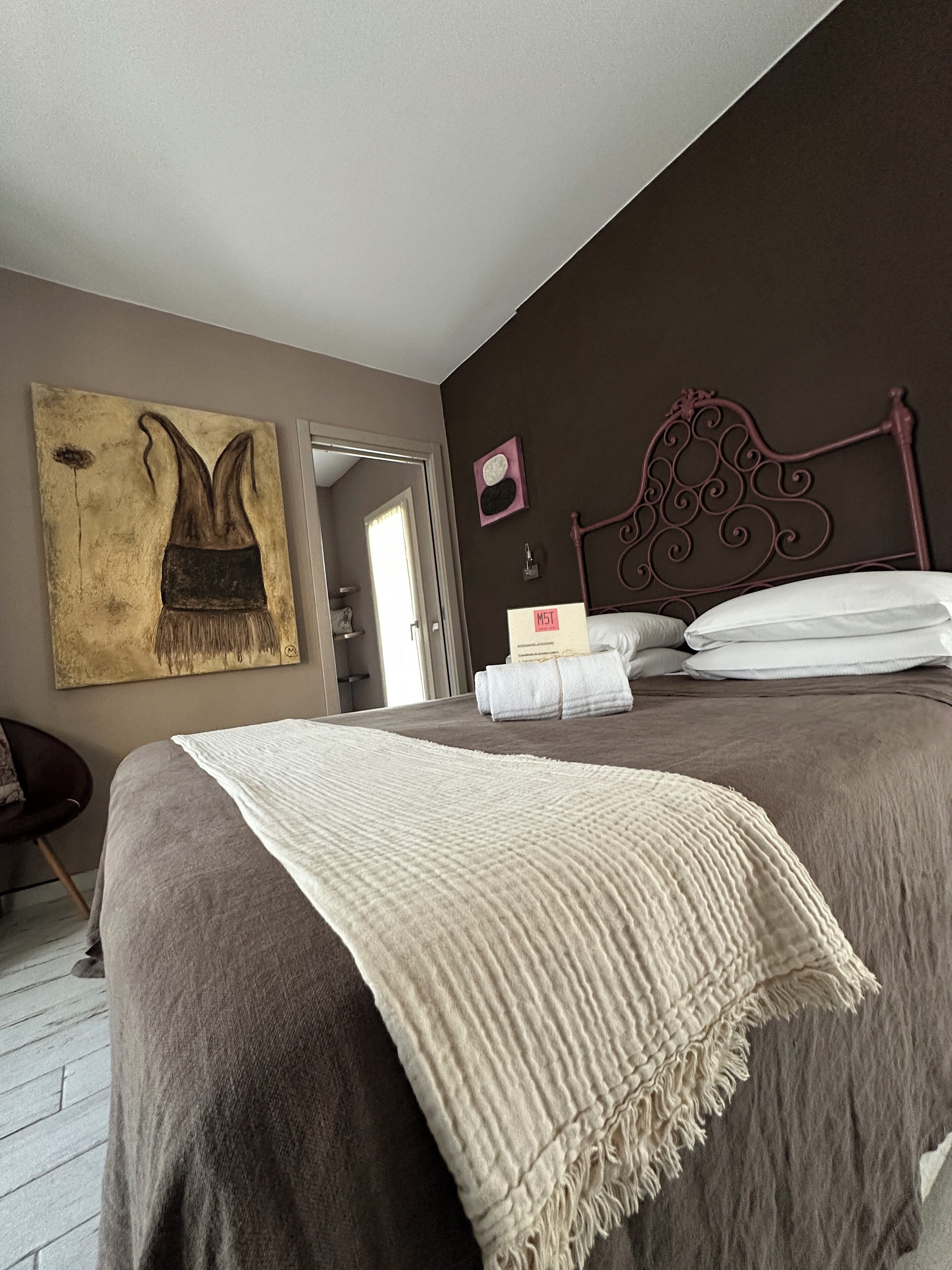Une chambre d’hôtel avec un lit, une tête de lit, un tableau et une porte donnant sur une salle de bain.