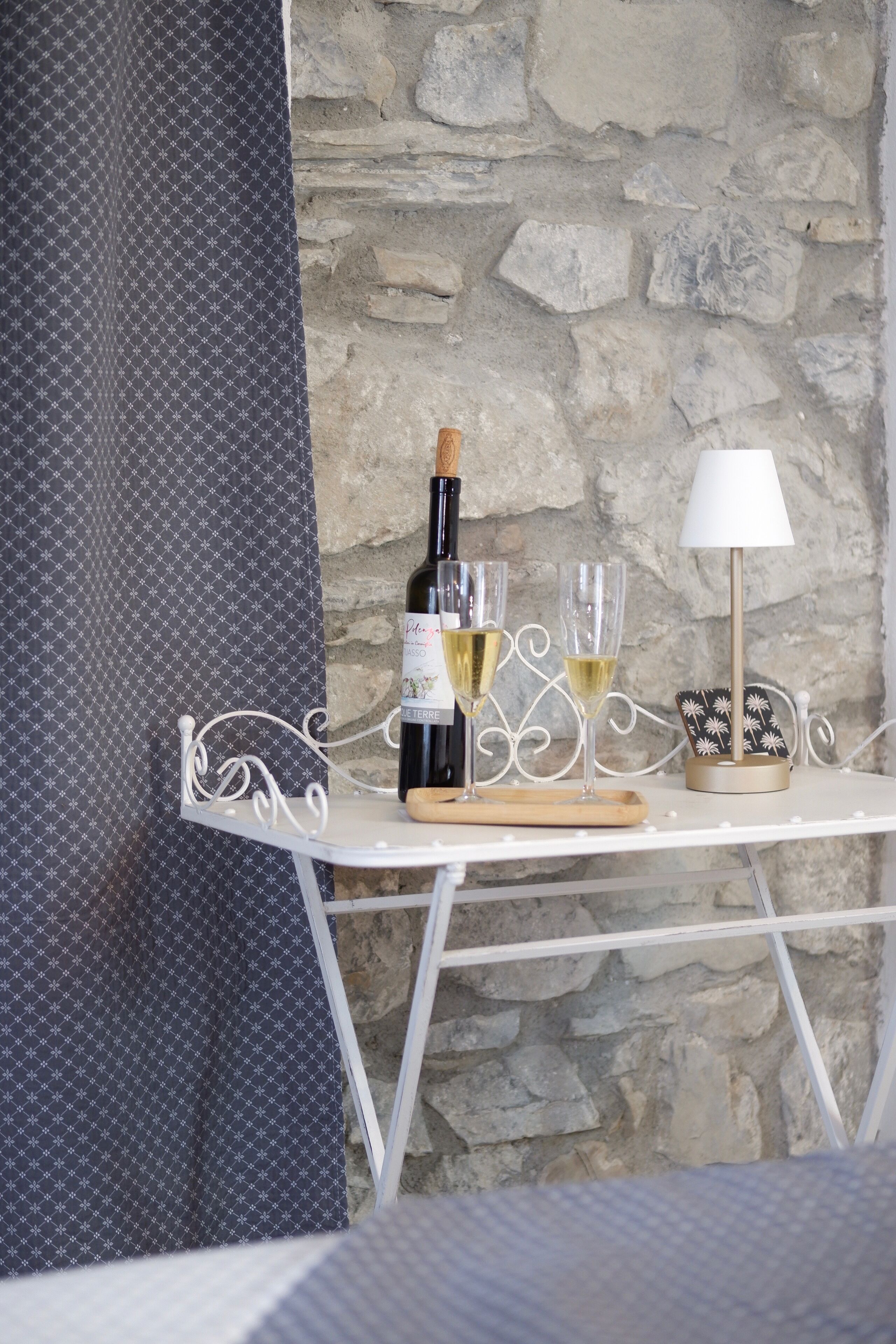 A table with a bottle of wine, two glasses, a candle holder, and a patterned curtain.