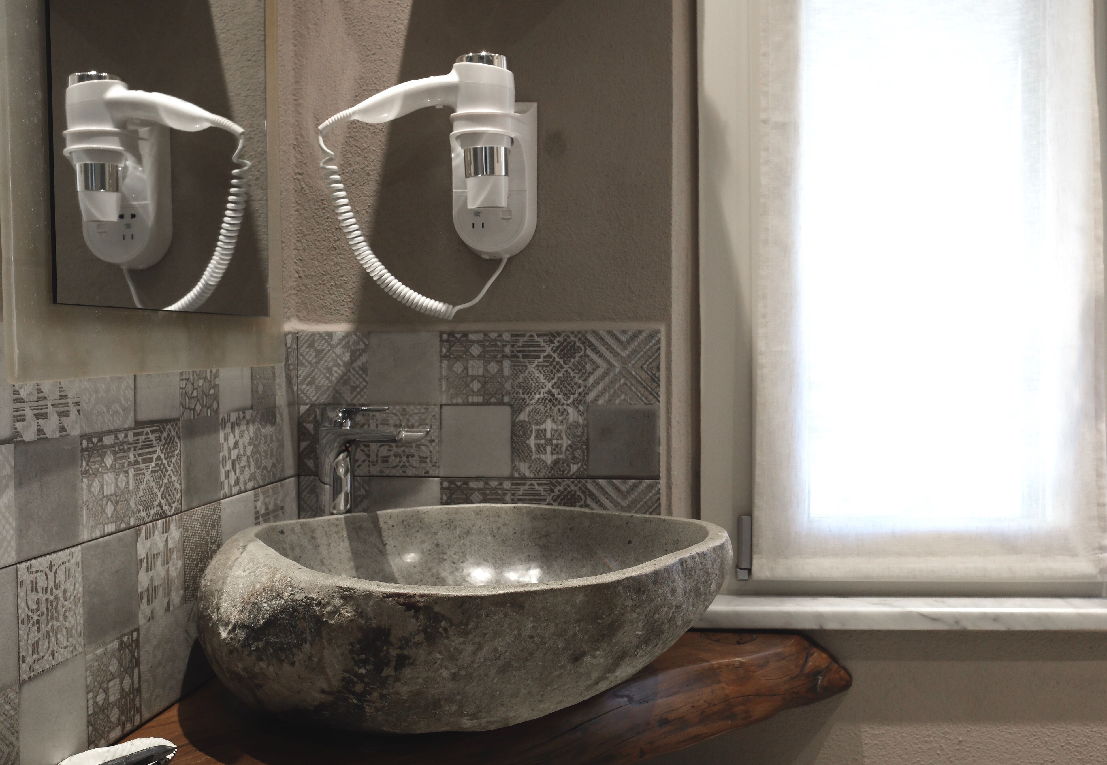 A bathroom with a large stone sink, a mirror with two hair dryers mounted on the wall, and patterned tiles.