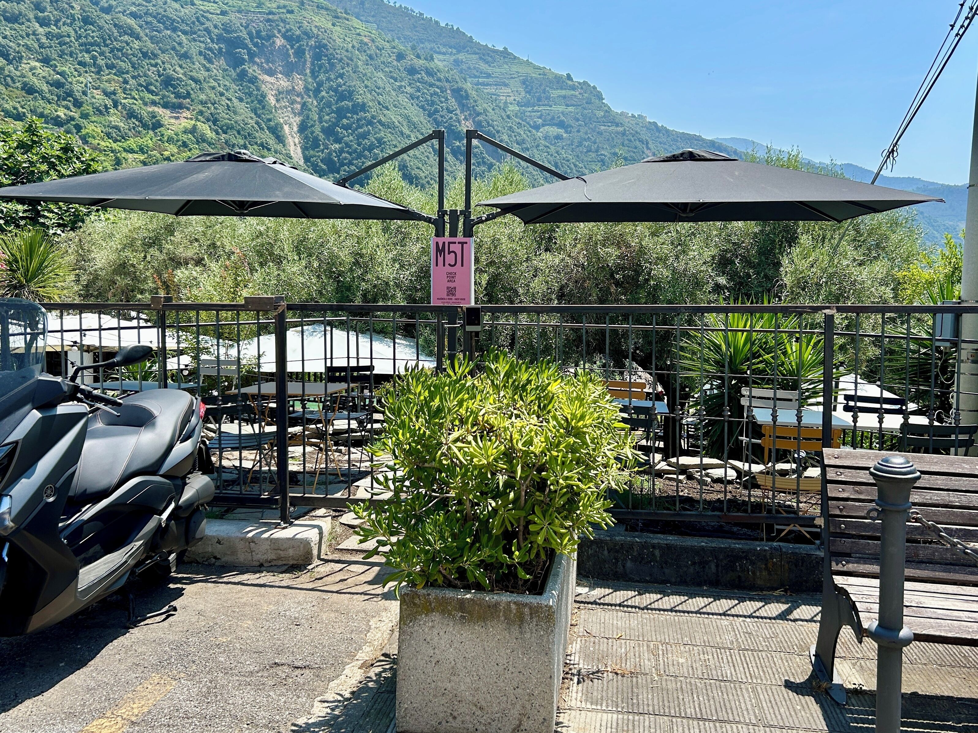 A parking area with a motorcycle, outdoor seating, and a sign indicating a check-in area.