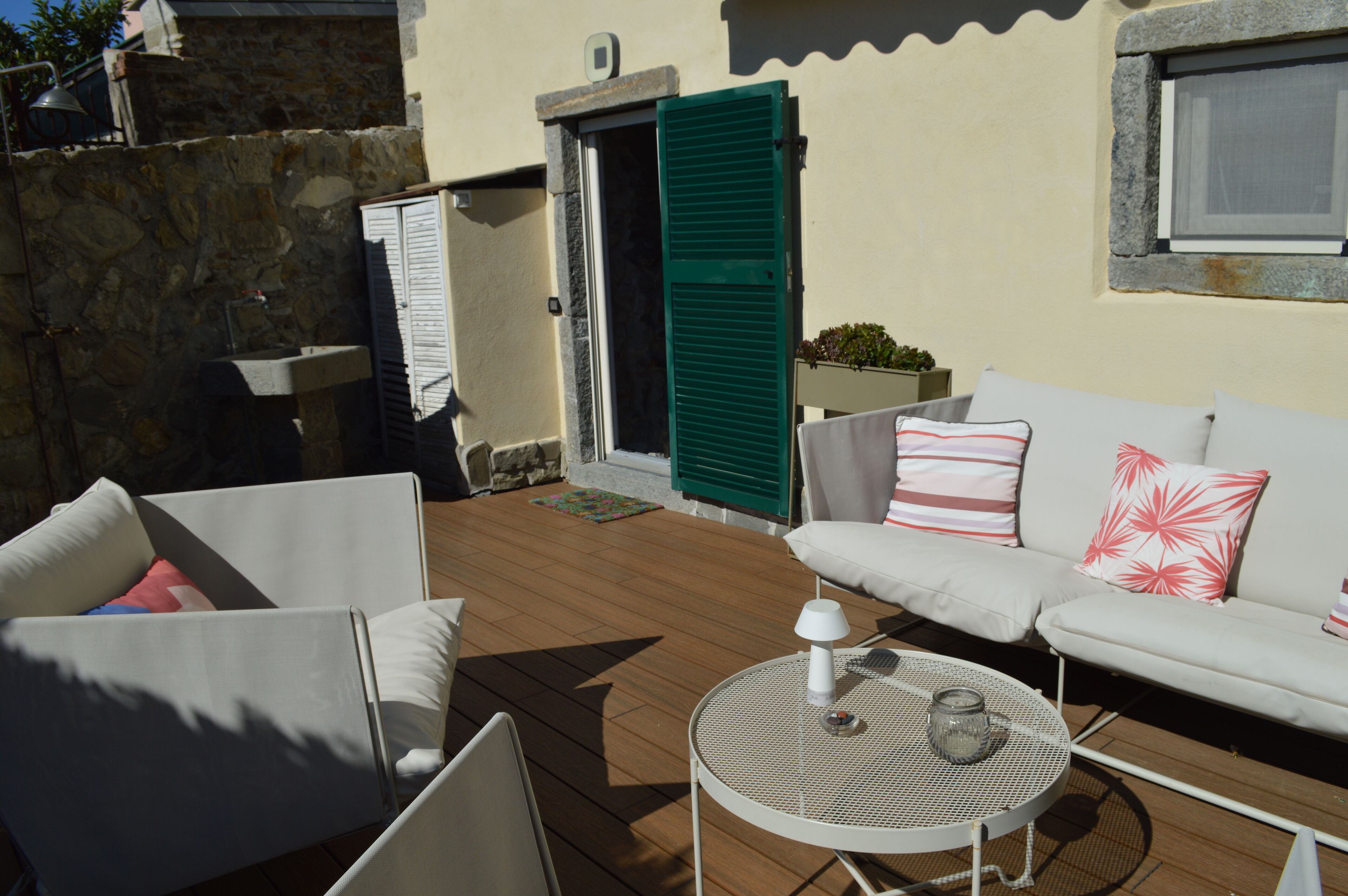 An outdoor seating area with a white sofa, two white chairs, and a round metal table.