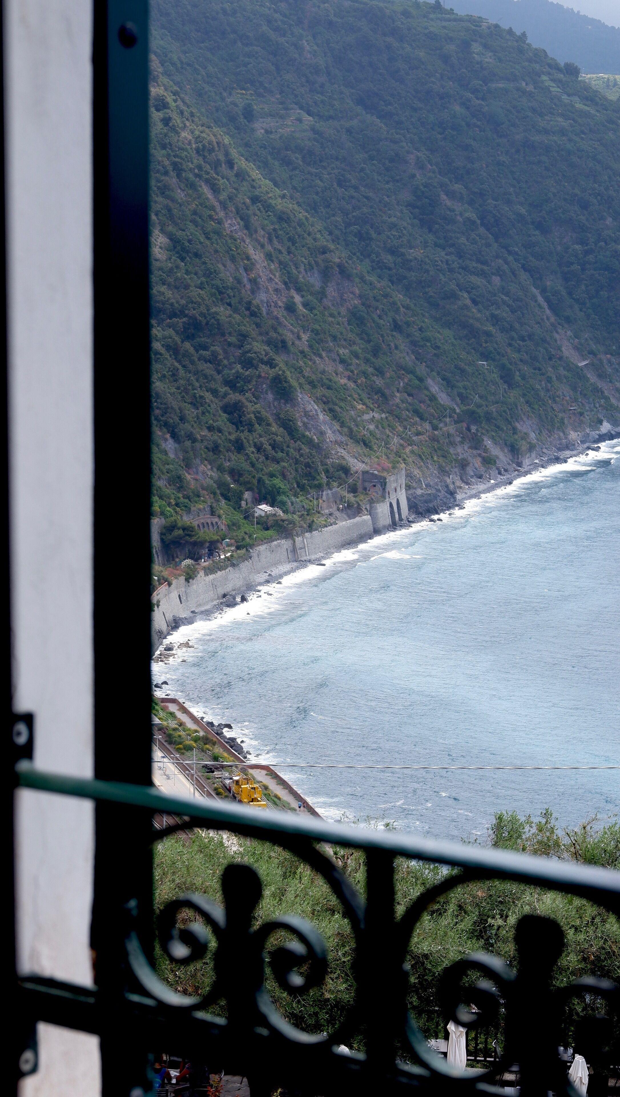 A coastal view with a rocky shoreline, a paved path, and a distant building.