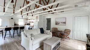 Ein geräumiger Wohnbereich mit einem weißen Sofa, zwei Korbstühlen, einem Couchtisch und einer Küche im Hintergrund.