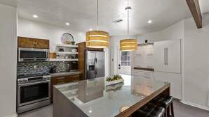 Une cuisine moderne dotée d’un îlot central, d’appareils électroménagers en acier inoxydable et de luminaires suspendus.