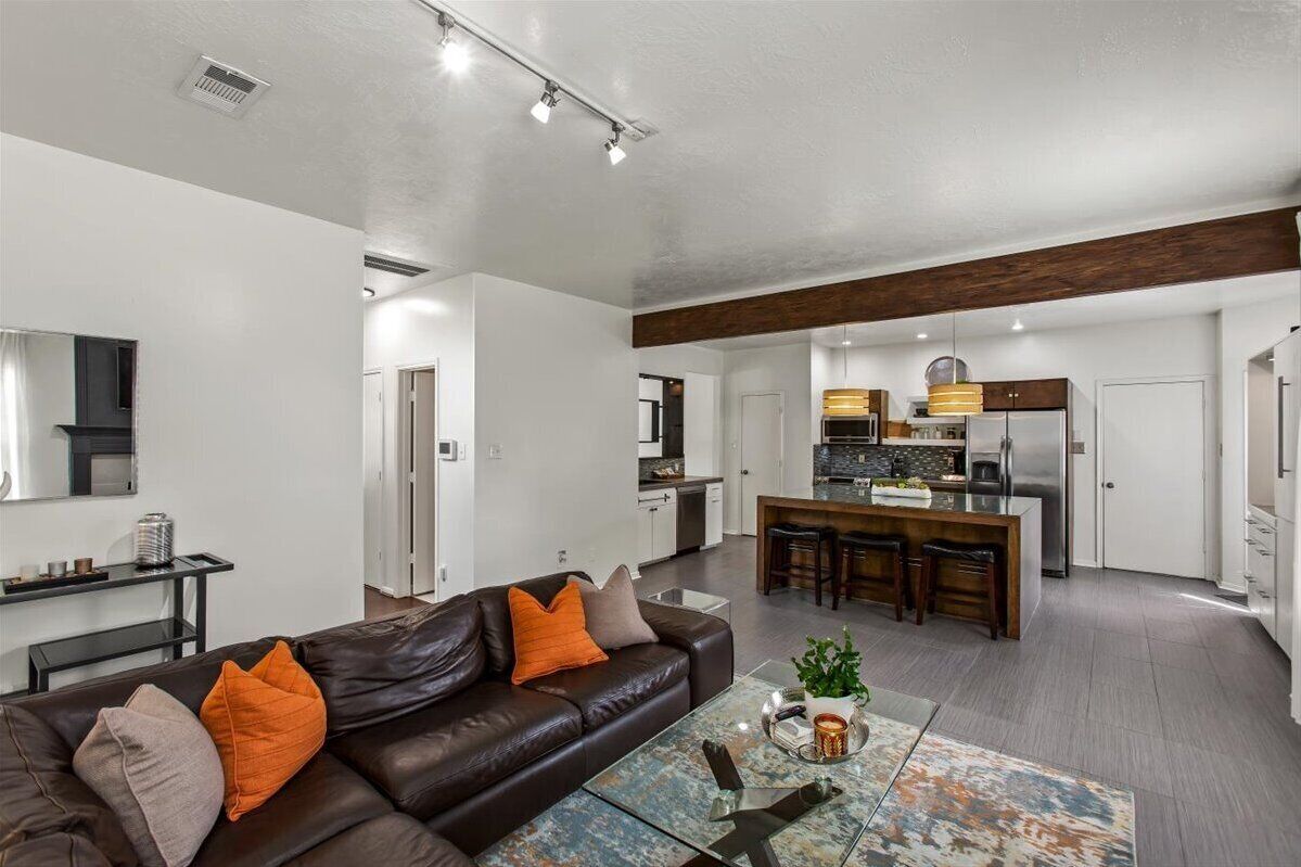 A modern living room with a leather sofa, a glass coffee table, and a kitchen in the background.