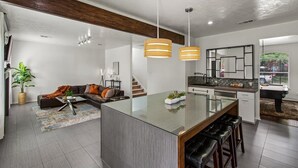 Une cuisine moderne dotée d’un îlot central, de luminaires suspendus et offrant une vue sur l’extérieur.