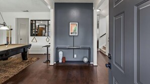 Un couloir moderne avec un mur gris foncé, un tableau encadré, une console ornée d’objets décoratifs et, au fond, une table de billard.