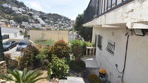 A residential area with a white building, a balcony, and a view of a hillside with houses.