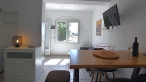 A modern kitchen with a dining table, a television mounted on the wall, and a window providing natural light.