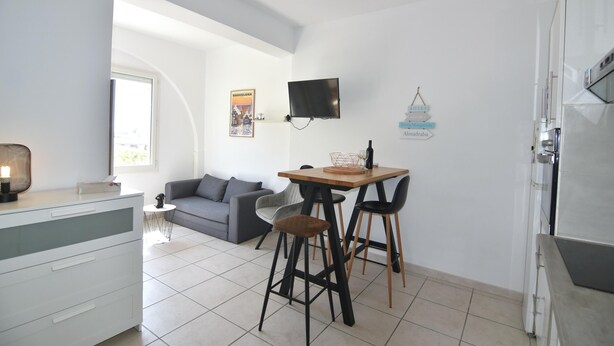 A modern kitchen with a dining area, a TV mounted on the wall, and a small table with chairs.
