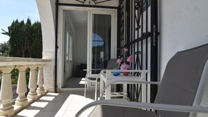 A balcony with a white chair, a small table with a flower vase, and a black metal gate.