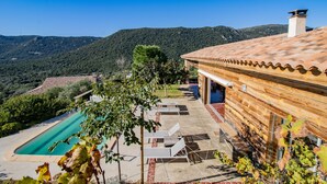 Ein Pool mit Liegestühlen, ein Gebäude aus Holz mit einem Ziegeldach und eine gebirgige Kulisse.