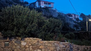 Ein Anwesen an einem Hang mit Steinmauern, einem Holzzaun und einem Haus mit einem Balkon.