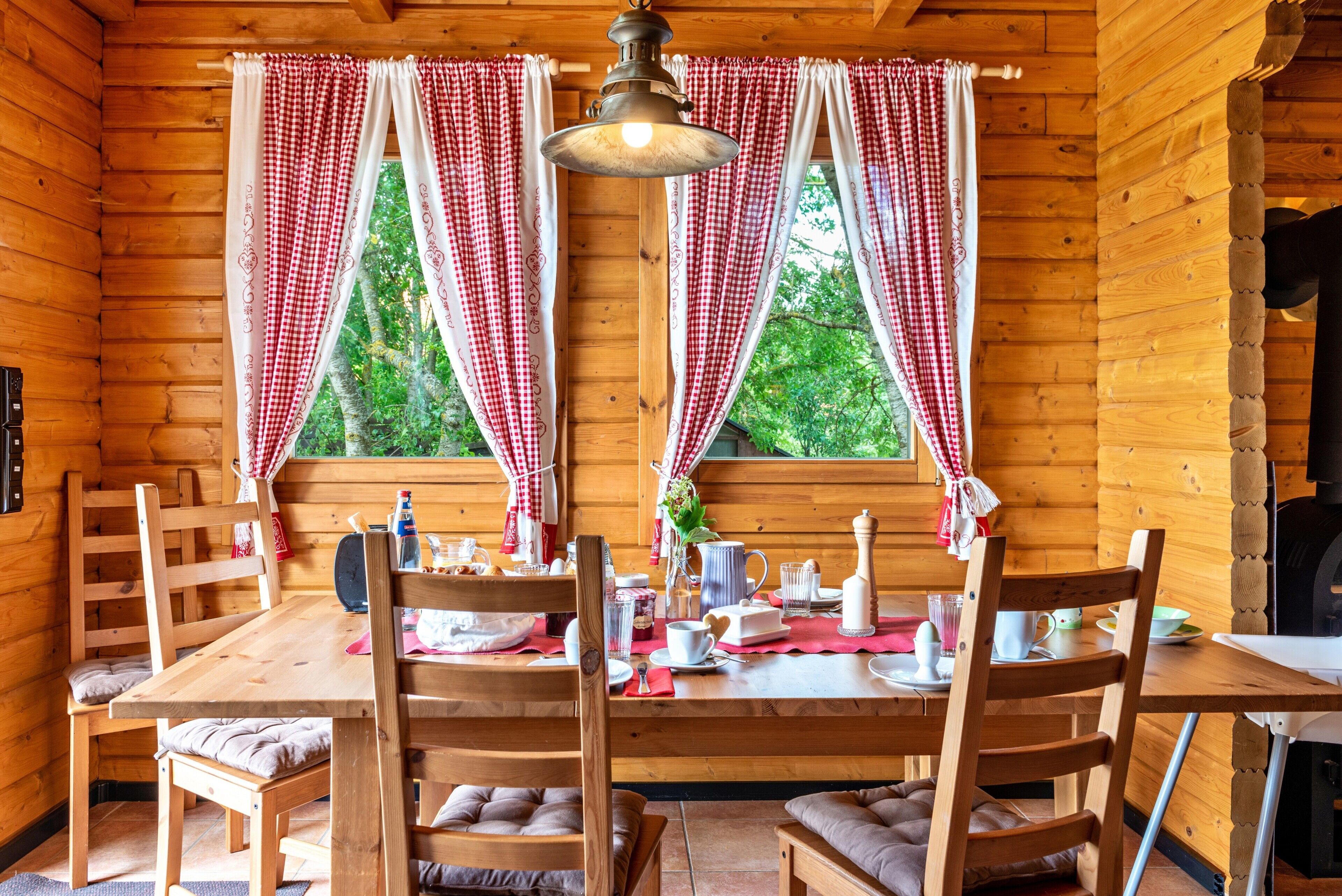 A wooden cabin interior with a dining table, chairs, and a hanging light fixture.