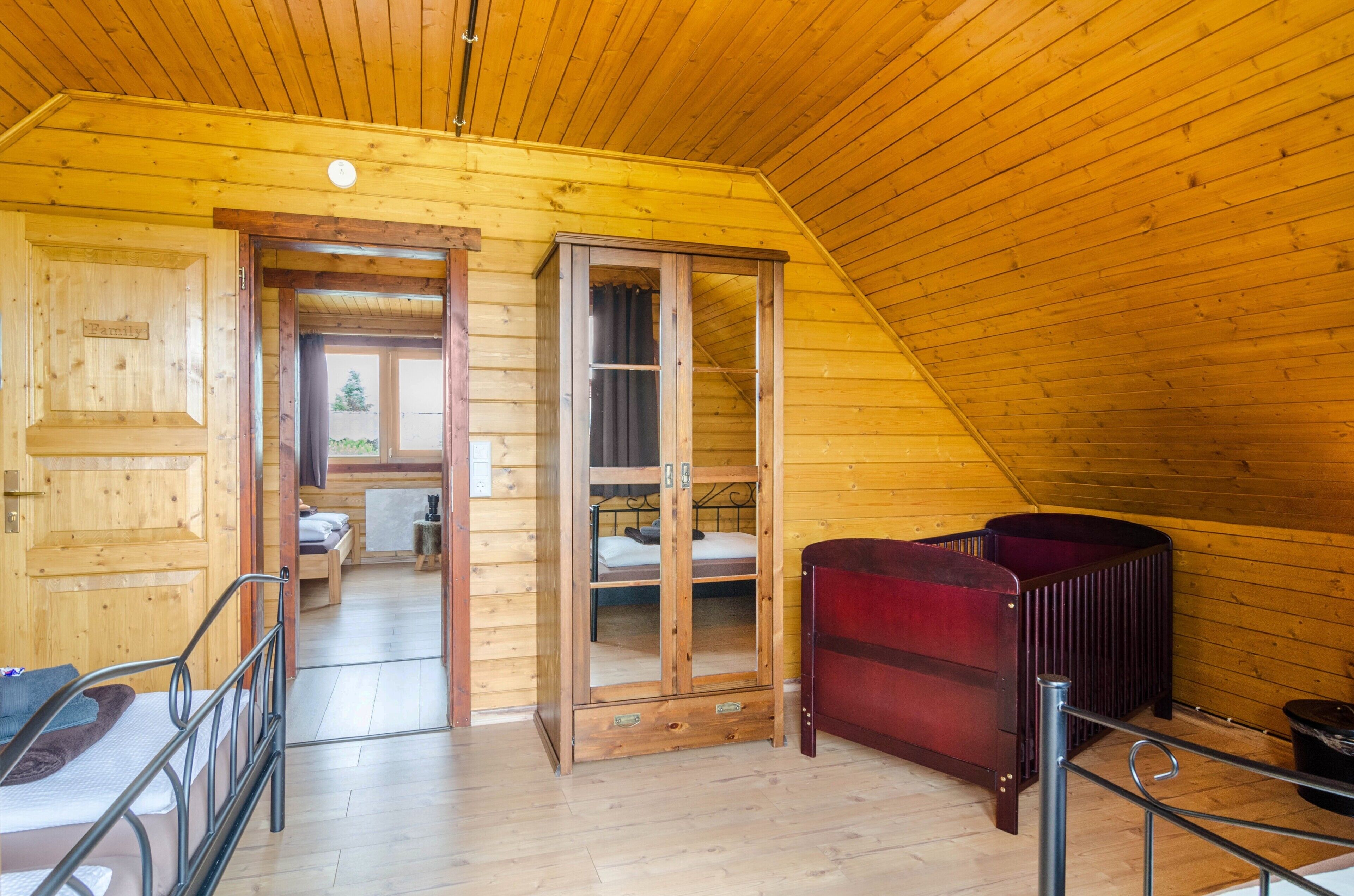 A wooden interior with a bed, a red cabinet, and a view through a door to another room.